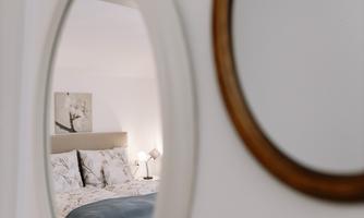 A cozy bedroom is seen in the mirror. It is well decorated with a bed, a pillow, and a lamp.