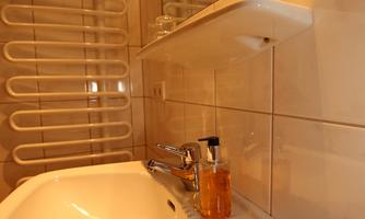 A modern bathroom with a white sink and a soap dispenser. The walls are brightly tiled and there is a transparent shower partition.