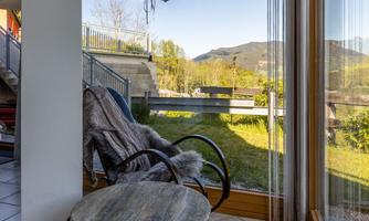 A cozy room with large windows that open up to the landscape. A stylish chair and a small table complement the relaxed atmosphere.