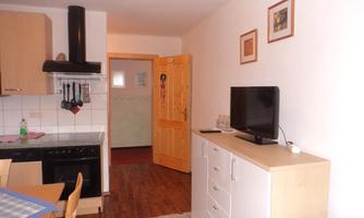 A cozy kitchen with wooden cabinets and a dining table. In the room, there is a television and bright walls.