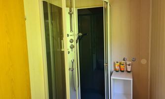 A stylish bathroom with a modern shower. Some skincare products are on a white shelf.