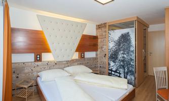 A modern bedroom with a cozy bed and a stylish headboard. The walls are made of wood, and a picture of a tree gives the room a natural touch.