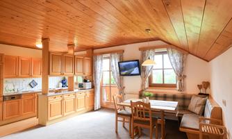 A cozy kitchen with wooden paneling and a dining area. The room has large windows and a television on the wall.