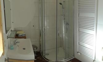 A modern bathroom with an open shower and a large mirror. There are bright tiles and some towels on the floor.