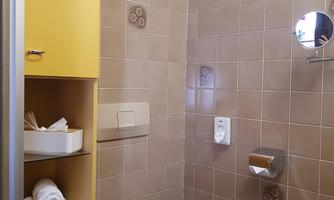 A small bathroom with brown tiles and yellow cabinets. There is a toilet, towels, and a mirror.