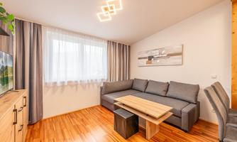 A modern living room with a gray sofa and a wooden coffee table. Large windows let in plenty of light, and the floor is made of wood.