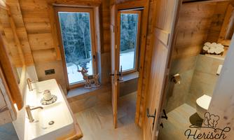 A modern bathroom made of wood with two sinks and large windows. The snow outside creates a cozy atmosphere.