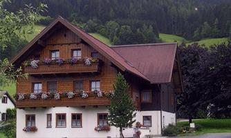 A traditional wooden house with colorful flowers on the balconies. Surrounded by green hills and trees.