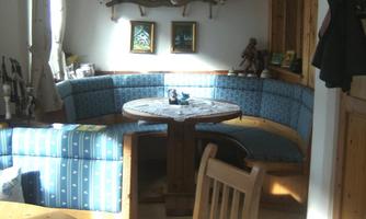 A cozy seating area with blue cushions and a round table. Bright walls and wooden details create a warm atmosphere.