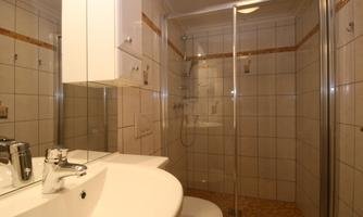 A modern bathroom with a shower cabin and an elegant sink. The walls are brightly tiled, with a clean and tidy design.