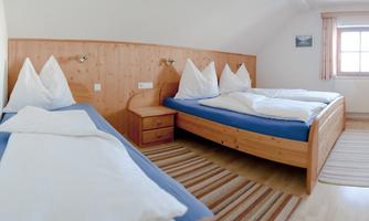 A cozy bedroom with two beds and a single bed. The walls are made of wood, and there is a carpet on the floor.