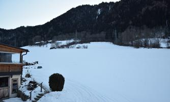 A snowy landscape with mountains in the background. In the foreground stands a rustic house and a frozen surface stretches far across the image.