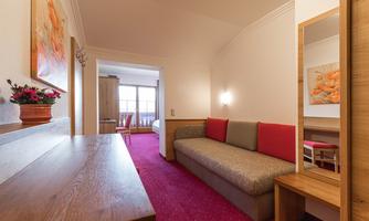 A cozy living area with a couch and a wooden table. The room has bright colors and access to another room.
