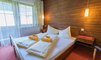 A cozy bedroom with a large bed and two towels. The room has wood paneling and large windows that let in plenty of light.