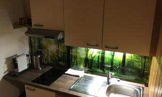 A modern kitchen with light cabinets and a wooden countertop. The backsplash features a green forest motif.