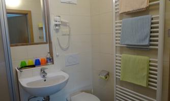 A small bathroom with a sink, a toilet, and a towel warmer. Colorful cups are on the sink, while fresh towels hang on the wall.