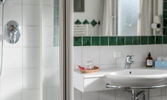 A modern bathroom with a shower and a sink. The green tiles give the room a fresh touch.