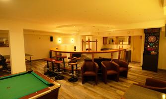 A cozy recreation area with a billiard table and a bar. The room has warm lighting and space for social gatherings.