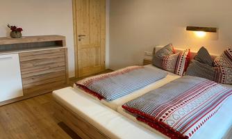 A cozy bedroom with a large double bed and decorative pillows. The room has a warm wooden floor and a modern dresser.