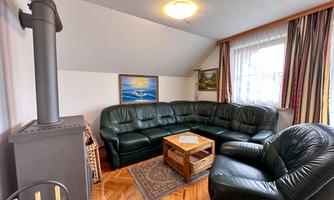 A cozy living room with a green leather couch and a small table. Some pictures hang on the wall, and a stove is in the corner.
