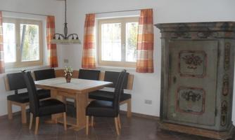 A bright dining room with a wooden table and six chairs. A decorative cabinet in vintage style stands against the wall.
