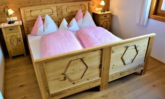 A cozy bedroom with a large wooden bed and pink bedding. Next to the bed are nightstands with lamps.
