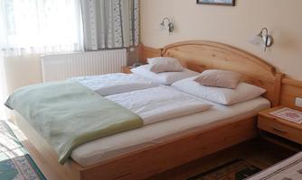 A cozy bedroom with a double bed and a red sofa. The room has bright colors and plenty of natural light.
