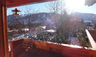 A sunny view from a balcony of snow-covered mountains and houses. The clear sky and rays of the sun create an inviting atmosphere.
