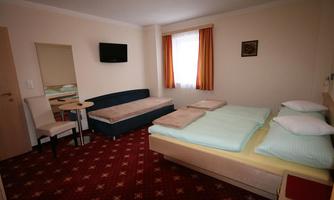 A simply furnished room with a double bed, a sofa, and a table. The room has a television and a window with curtains.