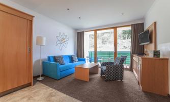 A modern living room with a blue sofa and a wooden table. Large windows offer a view of the landscape.