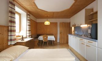 A cozy room with a double bed and a small dining area. The warm wooden tones and the windows create an inviting atmosphere.