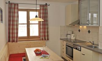 A modern kitchen with wooden beams and a dining area. The table is made of wood and has red chairs as well as a cozy seating area.