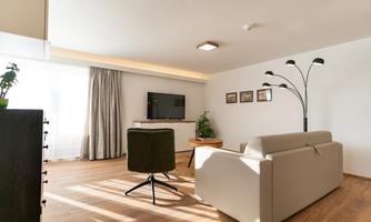 A modern living room with a large television, a comfortable sofa, and a stylish floor lamp. The large windows let in plenty of light and create a bright, inviting atmosphere.