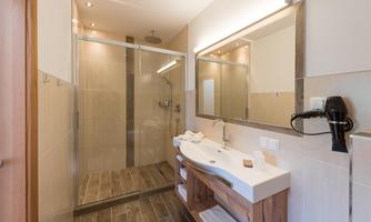 A modern bathroom with a shower and a large mirror. It features wooden elements and bright tiles.