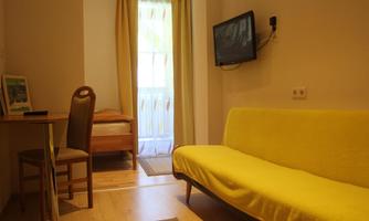 A simple room with a yellow sofa and a table.  
Windows with curtains and a television on the wall.