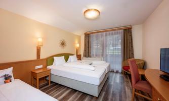 A cozy room with two beds and a desk. Large windows let in plenty of daylight and create a bright atmosphere.