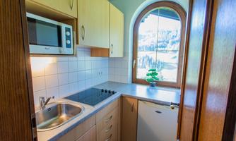 A small kitchen with modern appliances and a large window opening. The room is bright and friendly, with a view of the outdoor landscape.