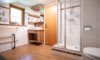A modern bathroom with a shower, a sink, and a toilet area. The floor is made of wood and the walls are tiled in a light color.