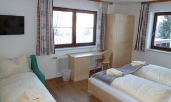 A bright and cheerful room with two beds and a green armchair. There is also a table and a television on the wall.