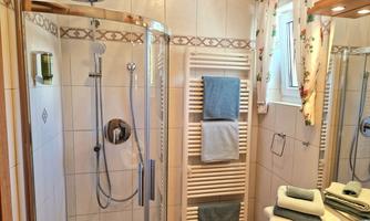 A bright bathroom with a shower and towels. The walls are tiled, and there is a large windowsill with natural light.