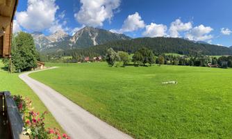 A picturesque landscape with green meadows and gentle hills. The sky is clear and the clouds are lightly scattered.