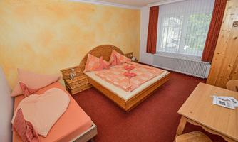 A cozy room with a double bed and a single bed. The walls are painted in warm colors and there is a table with chairs.