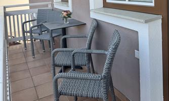 A cozy balcony with two rattan chairs and a small table. A flower vase is on the table.