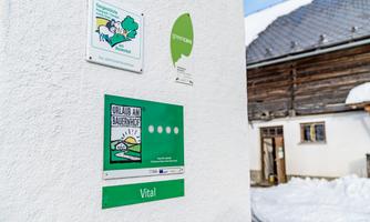 A white building wall with several signs, including a sign for a farm holiday. Snow can be seen on the ground.