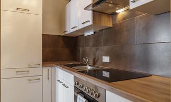 A modern kitchen with white cabinets and a wooden countertop. There is a stove, a sink, and a large work surface.