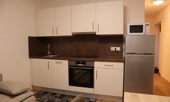 A modern kitchen with white cabinets and a dark countertop. It is equipped with a stove, a refrigerator, and a microwave.