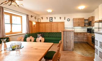A cozy kitchen with wooden furniture and a large table. The walls are decorated with gifts and wooden paneling.