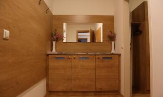 A bright hallway with wood paneling and a mirror above a console. Vases with flowers are on the console, and a door leads to another room.