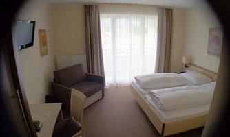A cozy hotel room with a double bed and a seating area. Large windows provide plenty of daylight.