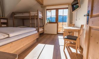 A cozy room with a bunk bed and a single bed. There is a desk and a nice view of the mountains through the window.